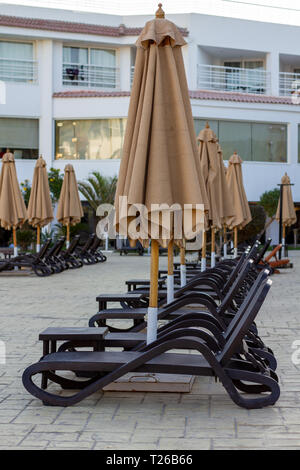 Several rows of empty beach loungers near the hotel swimming pool under closed umbrellas. Beach lounges, leaving in perspective. Empty sun loungers in Stock Photo