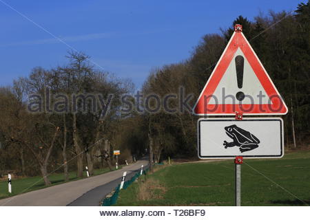 A triangular red sign warns drivers of the hazard of frogs crossing the road in spring Stock Photo