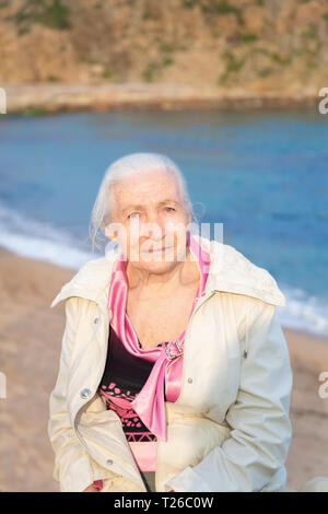 Portrait of the happy elderly woman against the sea in sunny spring day. Stock Photo