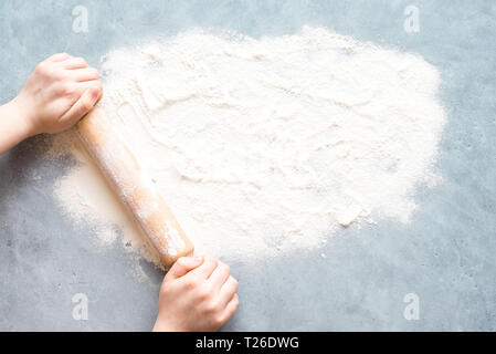 Flour and rolling pin in female hands on blue background, top view, copy space. Homemade baking concept, space for text. Stock Photo