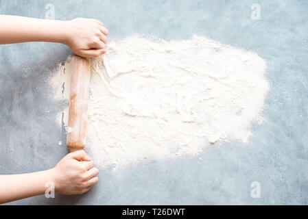 Flour and rolling pin in hands on blue background, top view, copy space. Homemade baking concept, space for text. Stock Photo