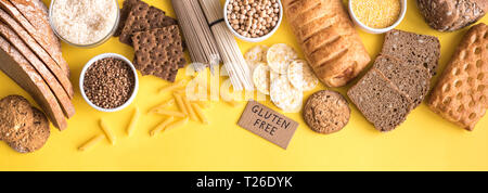 Gluten free food. Various gluten free pasta, bread, snacks and flour on yellow background, top view, banner. Stock Photo