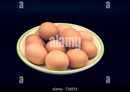 A dozen fresh brown eggs in a pottery dish isolated on a black background Stock Photo