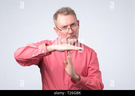 Senior man in red shirt giving showing time out hands gesture isolated on gray wall background Stock Photo