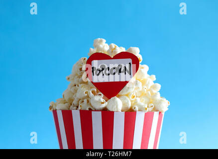 Delicious popcorn in classic red and white paper striped bag with label: I love Popcorn isolated on blue background. Stock Photo