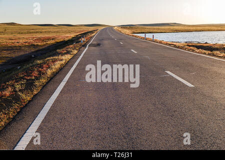 Asphalt road in Mongolian steppe along a small lake, Mongolia Stock Photo