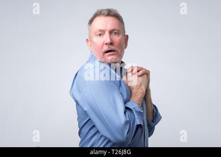 Senior greedy european man hides something in his hands and looks warily forward. Stock Photo