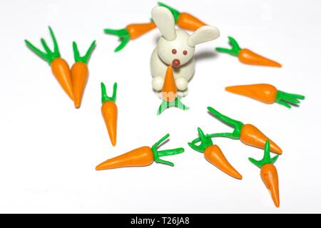 The white rabbit holds a carrot in its paws. A few carrots lie around the rabbit. The composition lies on a white background. Stock Photo