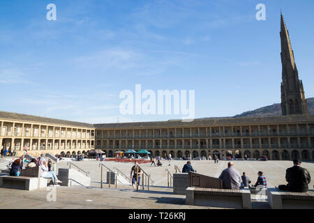 Visitors relax in The Piece Hall with Square Chapel church spire behind in the background. Sunny / sun & blue sky. Halifax, West Yorkshire, UK. (106) Stock Photo