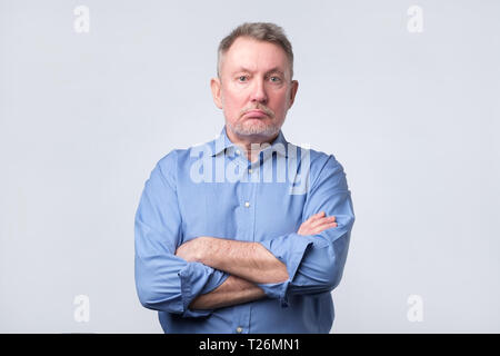 Serious senior man in blue shirt with folded arms and a deadpan expression. studio shoot Stock Photo