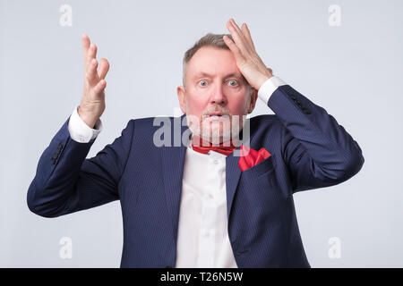 Senior caucasian man in blue shirt surprised with hand on head for mistake, remember error. Bad memory concept. Stock Photo