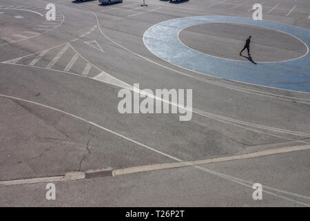 A man passing by a blue circle, Silhouette on a large parking lot area, Valencia Port Spain Stock Photo