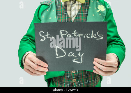 Cut view of man in green suit holding dark tablet with written words St. Patrick's day. Isolated on grey background Stock Photo