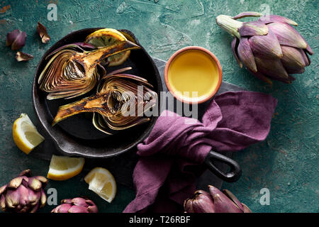 Flat lay with grilled and fresh red artishokes, whole and halved, on textured turquoise background Stock Photo