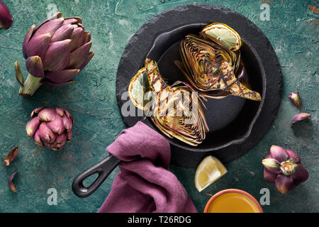 Flat lay with grilled and fresh red artishokes, whole and halved, on textured turquoise background Stock Photo