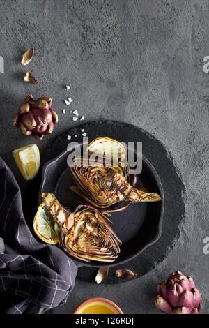 Flat lay with grilled and fresh red artishokes, whole and halved, on dark background, copy-space Stock Photo