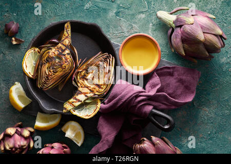 Flat lay with fresh and grilled red artishokes, whole and halved, on textured turquoise background Stock Photo