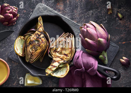 Flat lay with fresh and grilled red artishokes, whole and halved, on dark textured background Stock Photo