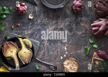 Flat lay with fresh red artishokes, whioe and halved, on dark background with copy-space Stock Photo