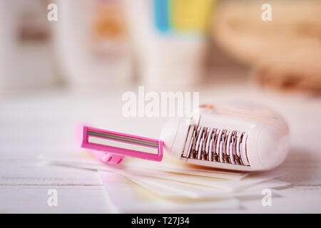 Epilator, shaving razor and wax strips on background with shampoo and towel, selective focus Stock Photo