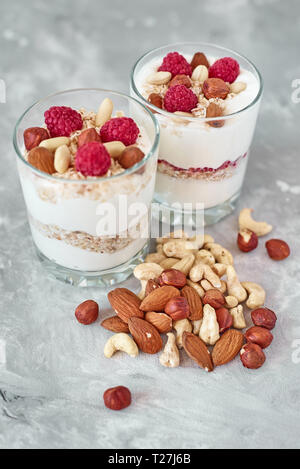 Two glasses of greek yogurt granola with raspberries, oatmeal flakes and nuts on white background. Healthy nutrition Stock Photo