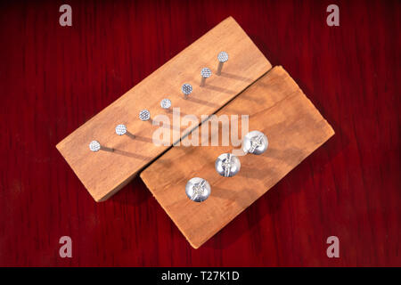 Three screws screwed into a piece of wood and seven nails stuck in a piece of wood too, on a wooden finish surface Stock Photo