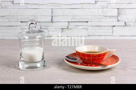 Orange colored cup of coffee with a modern design and a transparent sugar bowl on a white wooden table Stock Photo