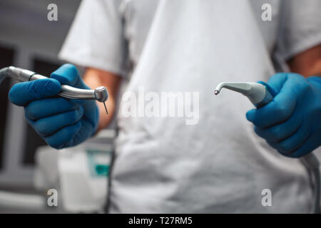 Close up and cut view of man's hands holding teeth equipment for treatment. He wear white robe. Hands covered with blue latex gloves. Stock Photo