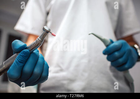 Close up cut view doctor's hands holding teeth equipment in hands for treatment. Man wear white robe and blue latex gloves. Stock Photo
