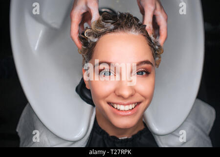 Top view of happy female customer smiling while hairdresser massaging hair. Young woman resting in beauty salon Stock Photo