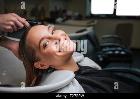 Beautiful young woman smiling and looking at camera while hairdresser rising hair after shampoo. Beauty and people concept Stock Photo