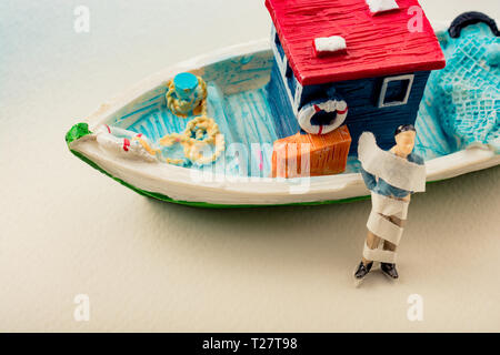 Tiny wrapped figurine of man model beside a model boat Stock Photo