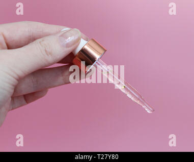 Pipette with gualinic liquid in a female hand. Serum with gold particles for the skin. Moisturize the skin with gold particles in the liquid. Female h Stock Photo