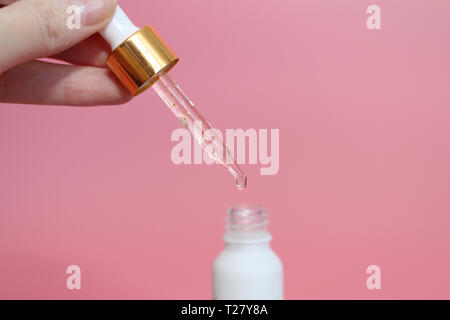 Pipette with liquid in which gold particles are visible. Serum with gold particles for the skin. Female hand holding a beautiful dropper with liquid.  Stock Photo