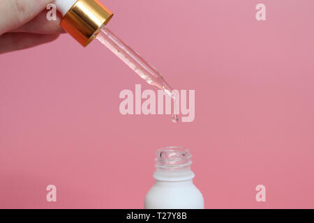 Pipette with liquid in which gold particles are visible. Serum with gold particles for the skin. Female hand holding a beautiful dropper with liquid.  Stock Photo