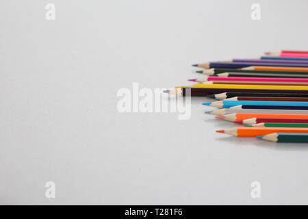 Color pencils for schoolchildren and students. Pencils are scattered on a white table and stand in a glass. Pencils for office workers. Stock Photo