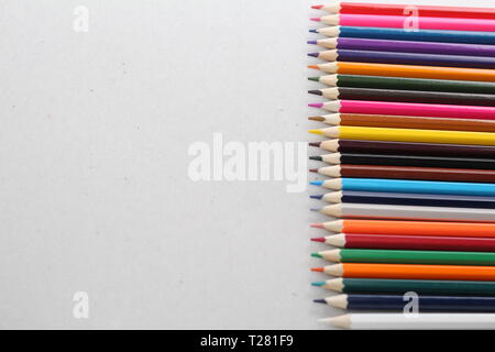 Color pencils for schoolchildren and students. Pencils are scattered on a white table and stand in a glass. Pencils for office workers. Stock Photo