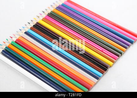 Color pencils for schoolchildren and students. Pencils are scattered on a white table and stand in a glass. Pencils for office workers. Stock Photo