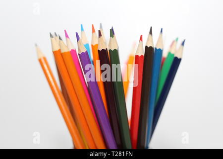 Color pencils for schoolchildren and students. Pencils are scattered on a white table and stand in a glass. Pencils for office workers. Stock Photo