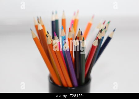 Color pencils for schoolchildren and students. Pencils are scattered on a white table and stand in a glass. Pencils for office workers. Stock Photo