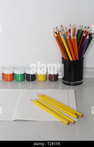 Color pencils for schoolchildren and students. Pencils are scattered on a white table and stand in a glass. Pencils for office workers. Stock Photo