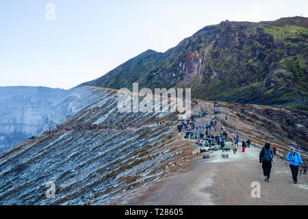 View of the Kawah Ijen volcanic crater with a crowd of tourists and sulfur miners at the edge. Java, Indonesia Stock Photo