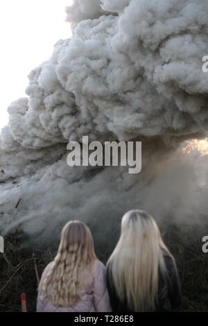 Two girls wathing a fire with heavy smoke. Celebrations of Valborgsmässoafton in Sweden. Swedish tradition. Stock Photo