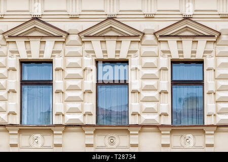 Three rectangular Windows with triangular cornices on a beige background of the wall with a bas-relief . From a series of windows of St. Petersburg. Stock Photo