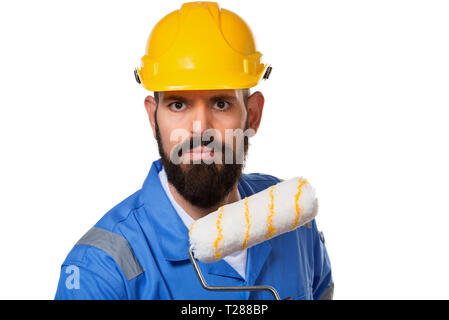 Bearded builder in yellow helmet and blue uniform holding paint roller. Isolated on white background. Stock Photo