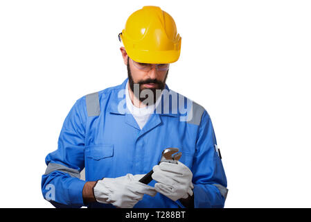 A man, a worker, in a yellow helmet and blui uniform looking at steel adjustable spanner, isolated over white background Stock Photo