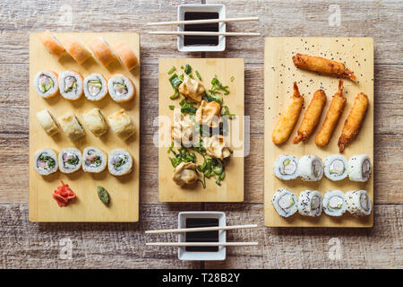 California sushi roll, sake sushi roll, fried shrimps, gyozas and soy sauce on a wooden table Stock Photo