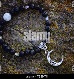 Black lava stone moon pendant bracelet on rocky background Stock Photo