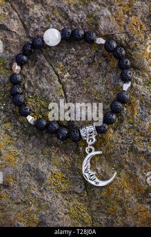 Black lava stone moon pendant bracelet on rocky background Stock Photo
