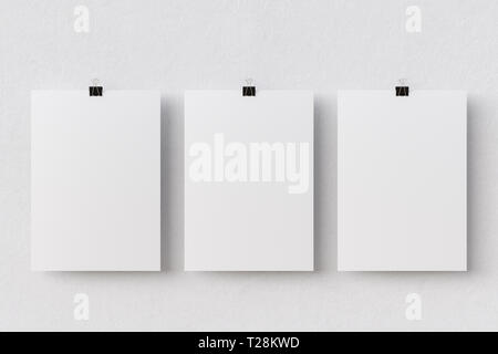 Three blank paper posters hanging on binder clips on white wall background Stock Photo